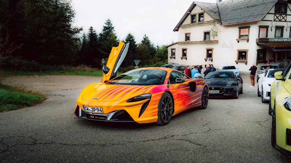 Orangefarbener McLaren mit geöffneten Türen beim Tourstopp