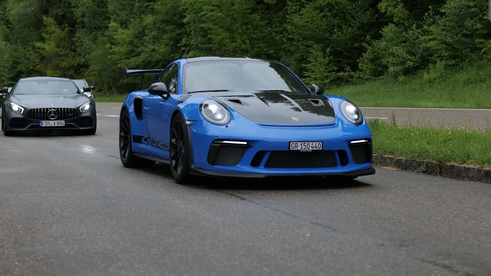 Blauer Porsche 911 GT3 RS mit folgendem Mercedes-AMG auf einer Waldstraße