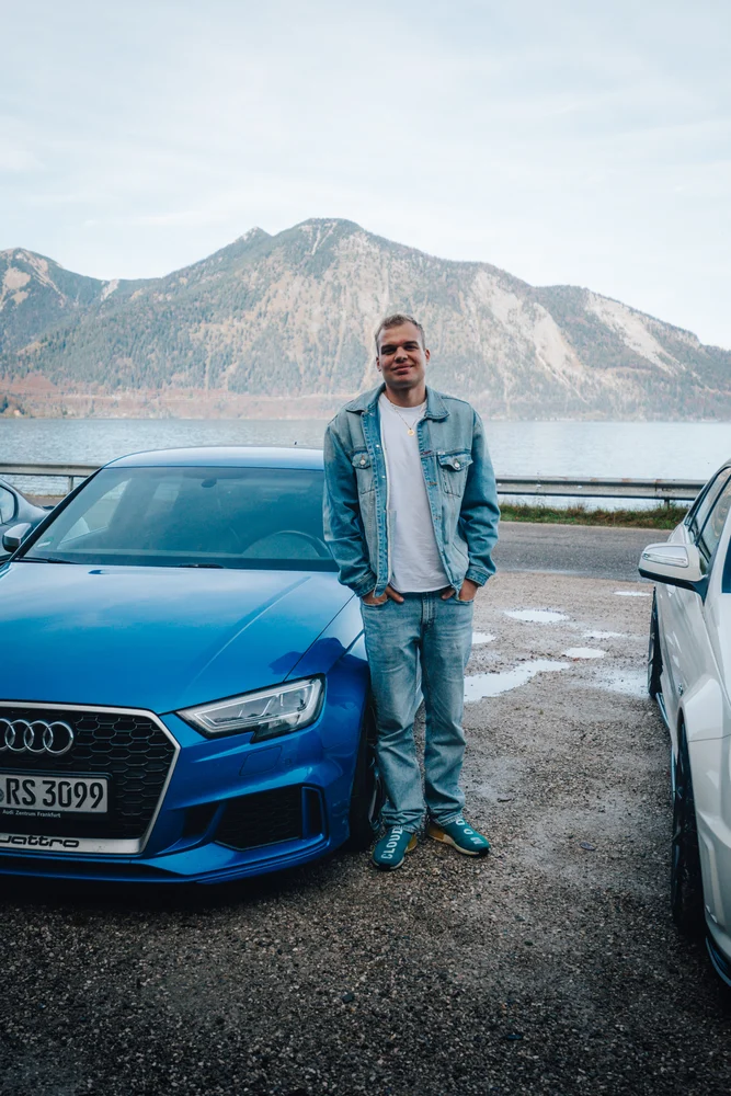 Teilnehmer mit blauem Audi am See vor dem Bergpanorama