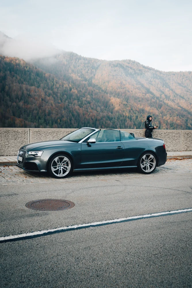 Dunkles Audi-Cabriolet am See vor den herbstlichen Bergen