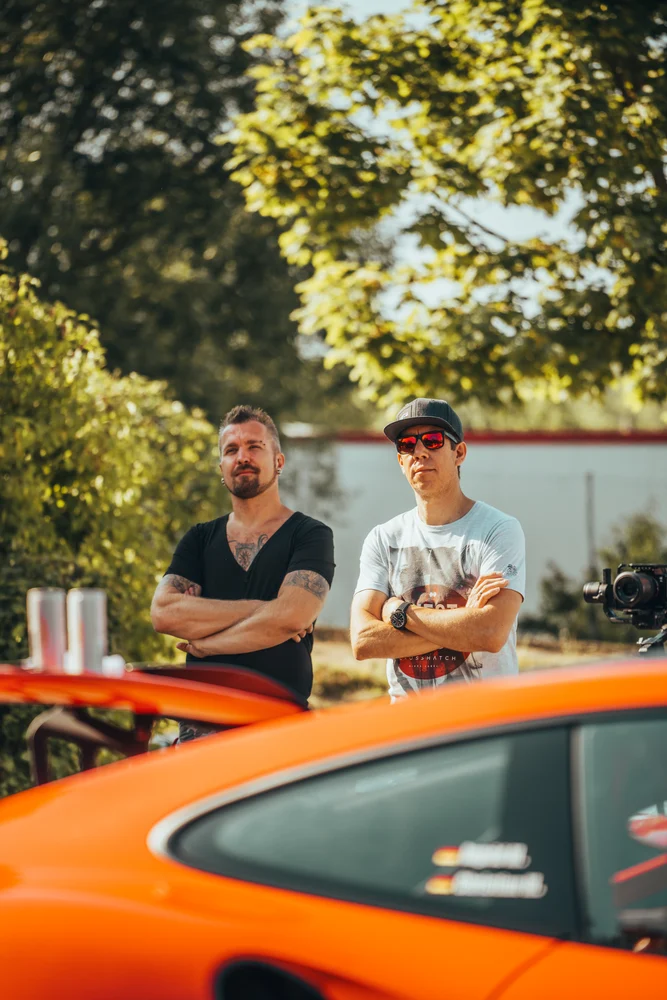 Zwei Teilnehmer beim Briefing hinter dem orangefarbenen Porsche