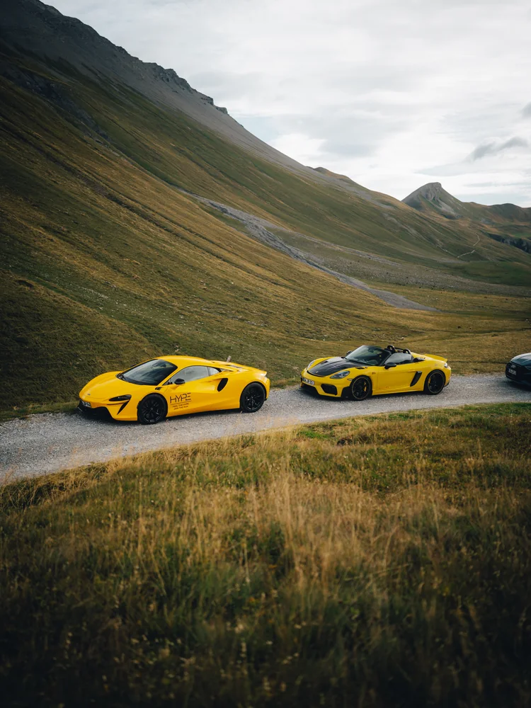 Gelber McLaren und Porsche Spyder RS auf einer Passstraße vor den Schweizer Alpen